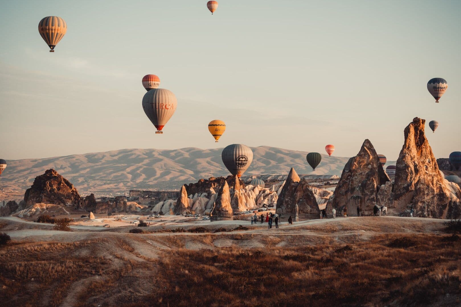 Hot air balloons rising over Cappadocia fairy chimneys at sunrise viewed from a rooftop terrace